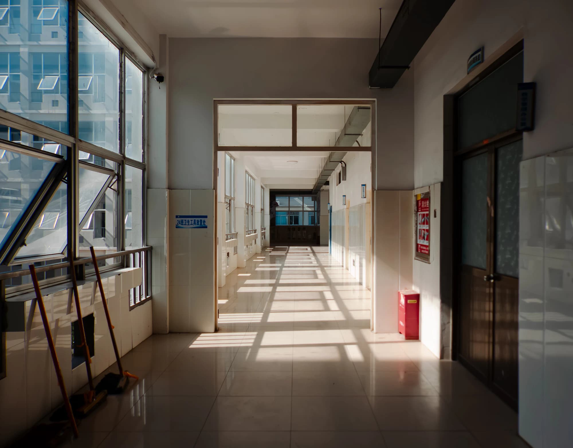 Sunlit school hallway with a mop resting in the corner