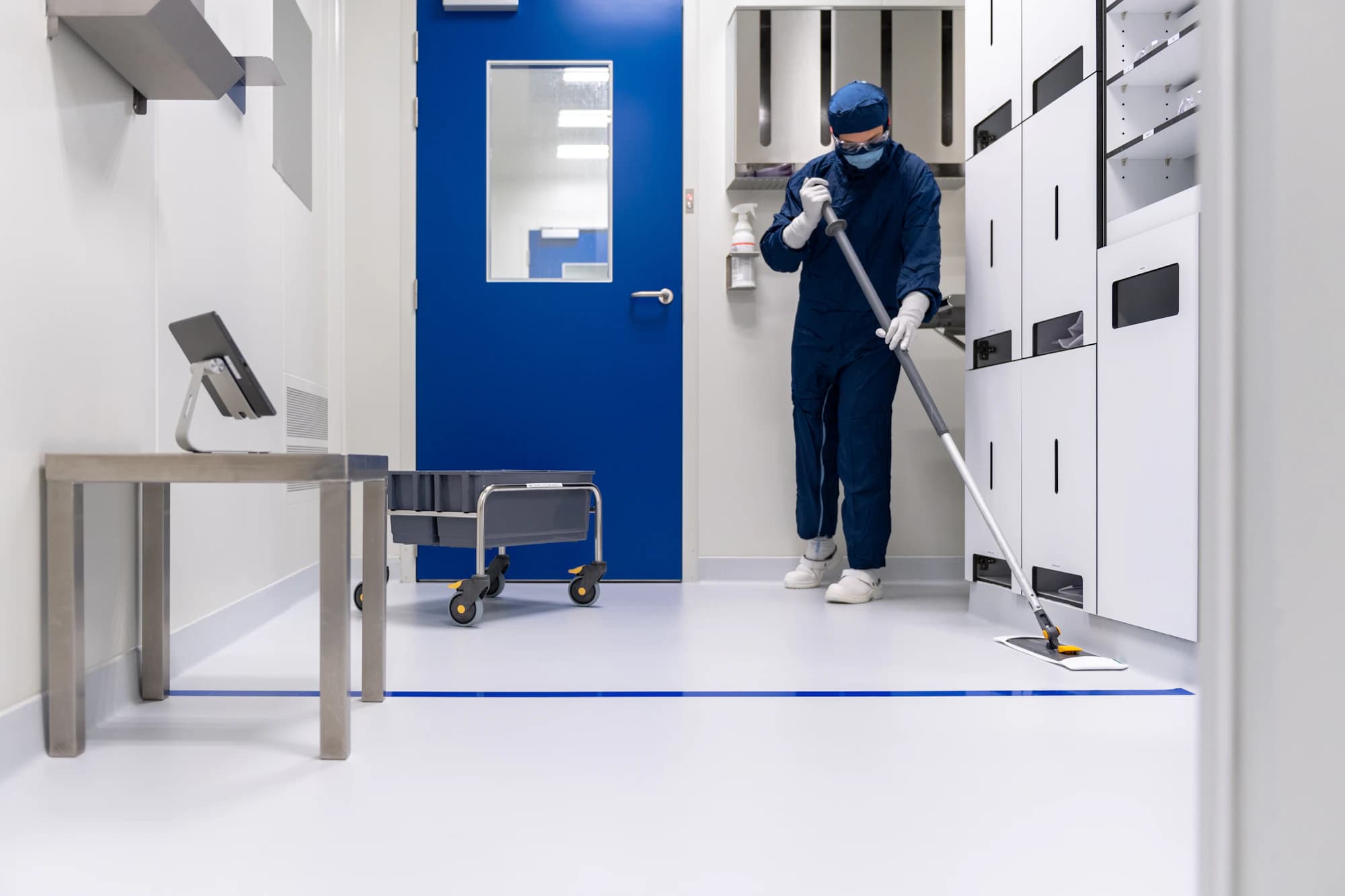 Cleaner in coveralls mopping a white clinical floor