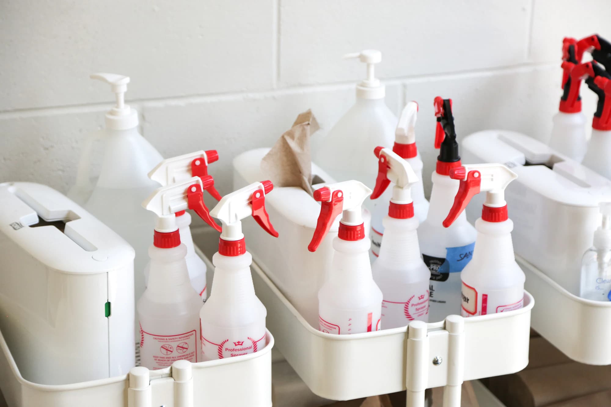 Spray bottles and soap dispensers lined up in supply caddies