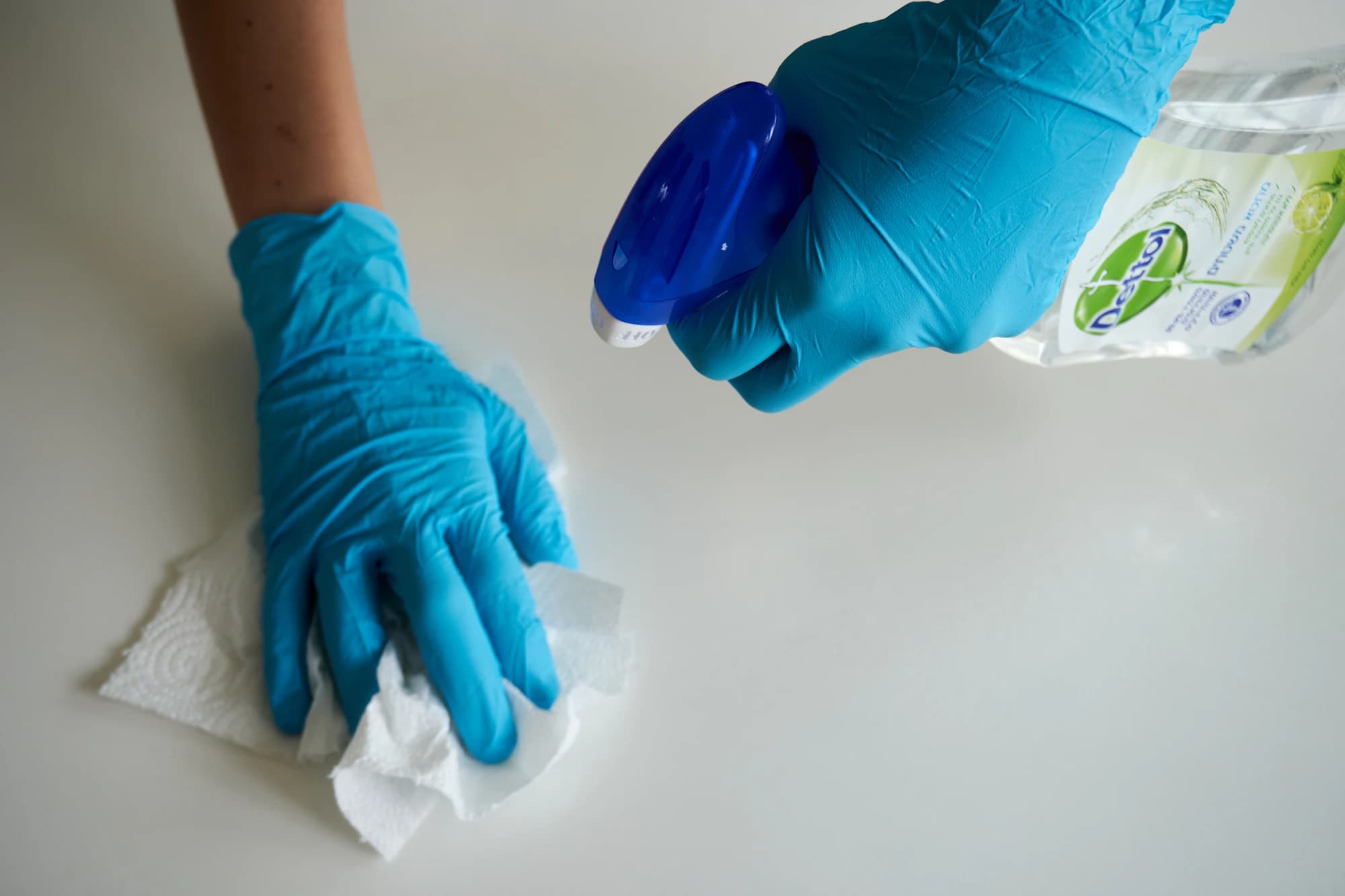 Gloved hands wiping a counter with disinfectant
